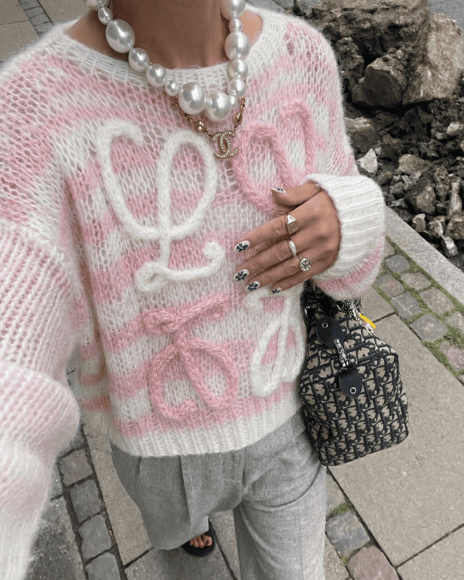 Close-up of the Blush Pink Loewe Knit styled with a large pearl necklace and grey trousers for a Parisian look.