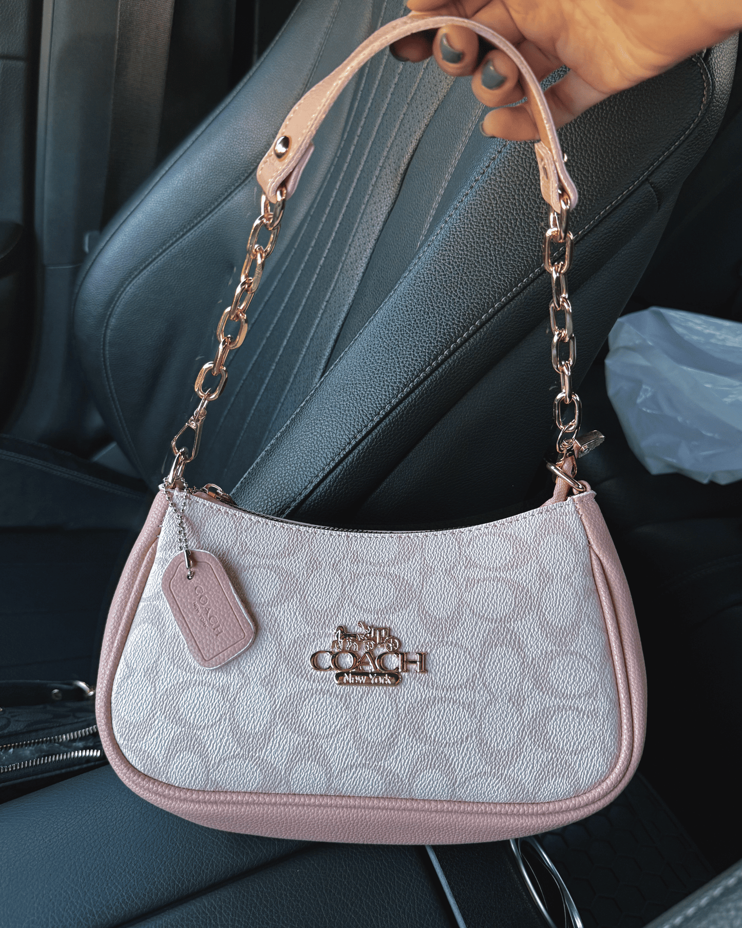 Close up of the pink inspired coach baguette bag being held, showing
the gold monogram detail.