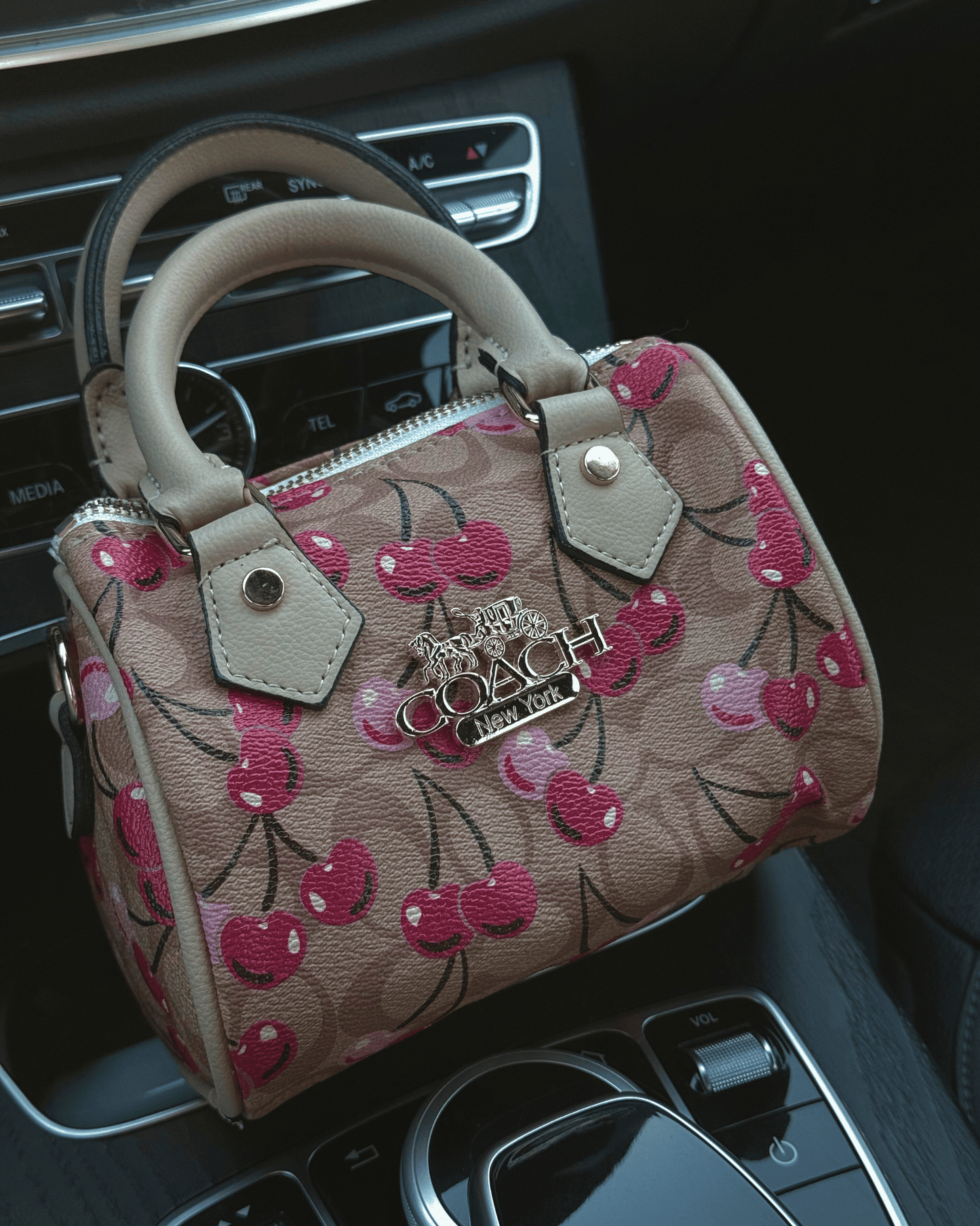 Mini beige coach pattern Inspo cherry print bag sitting in a luxury car interior, showing main-character energy aesthetic.