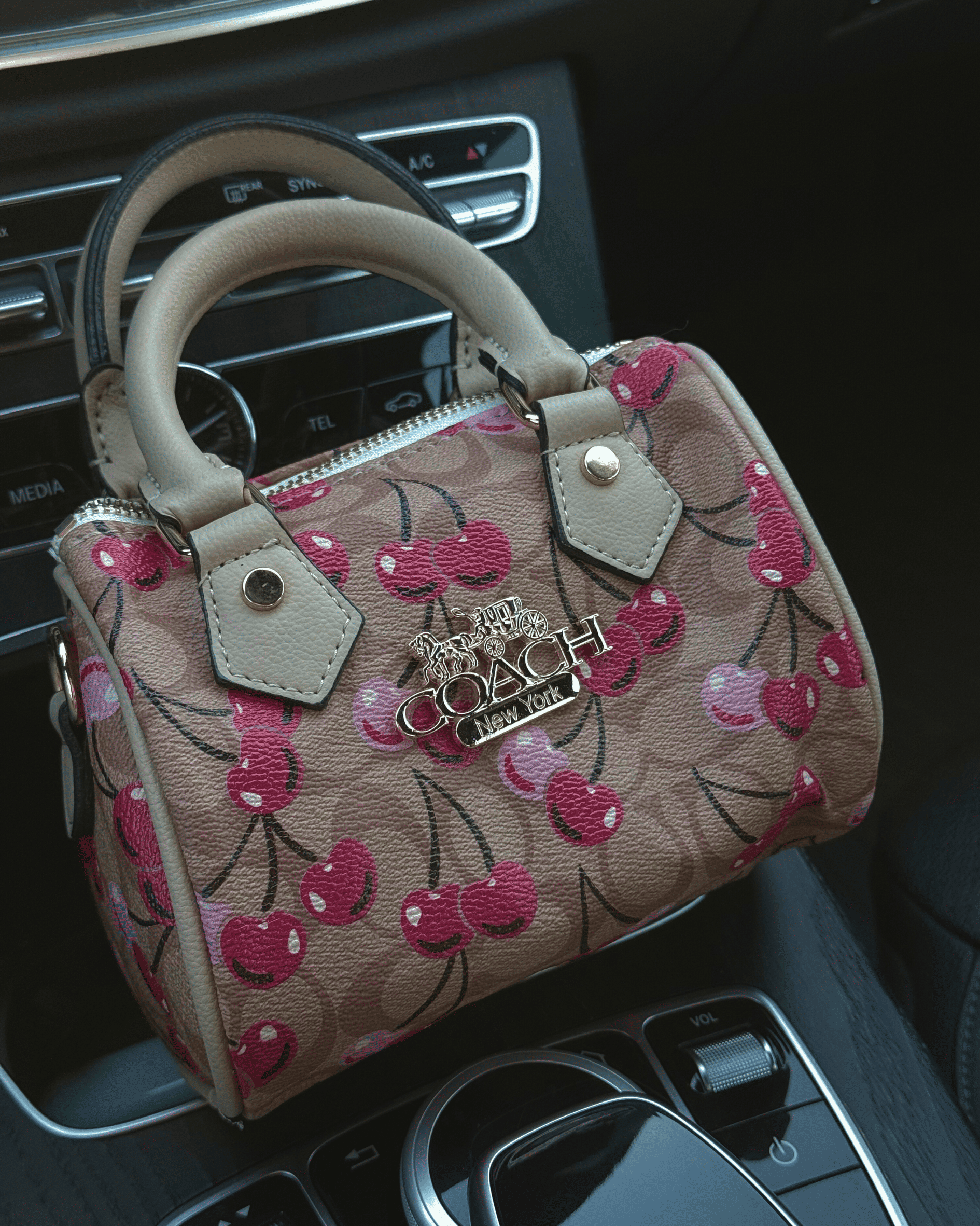 Mini beige coach pattern Inspo cherry print bag sitting in a luxury car interior, showing main-character energy aesthetic.