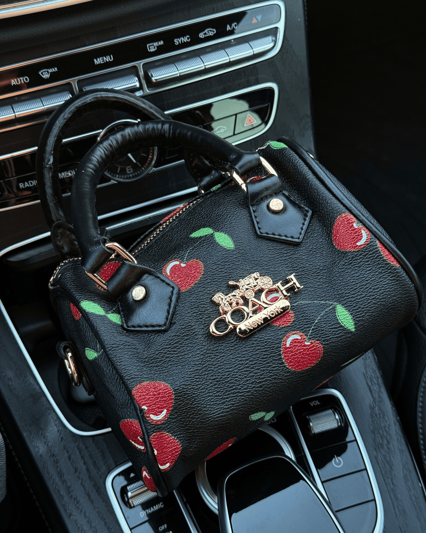 Black cherry print mini bag styled in a car, perfect for a high-end "it-girl" aesthetic.