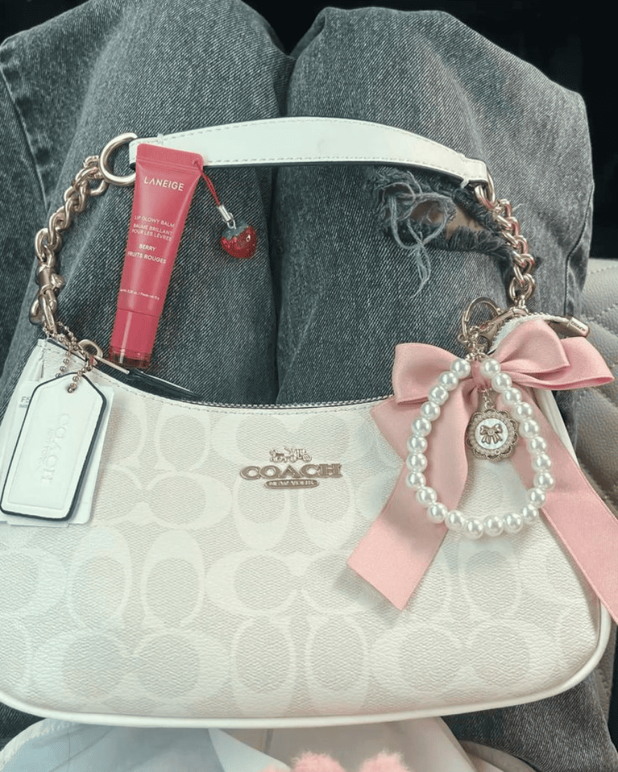 White monogram baguette bag styled with a pink satin bow and pearl charms for a coquette look.