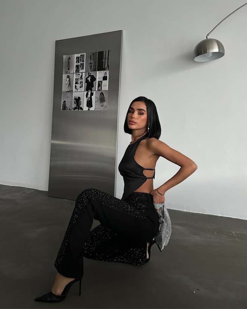 Side view of a model crouching in wide-leg washed black jeans with all-over crystal embellishments and black high heels, showcasing a high-glam streetwear look.