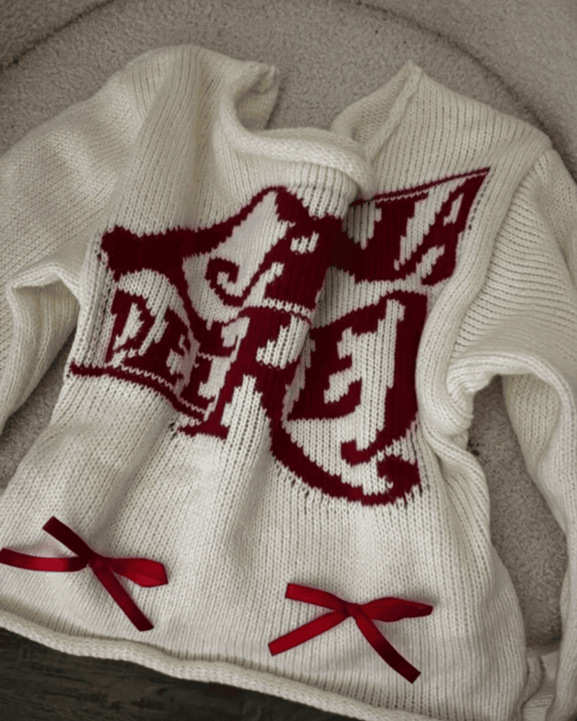  Folded off-white knit sweater showing red ribbon bow details and vintage inspired branding.